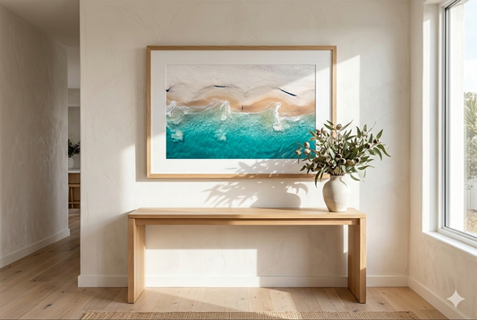 Framed artwork on a wall above a wooden console table with a vase of flowers.