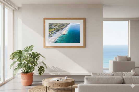 Framed artwork of a coastal scene in a modern living room with large windows.