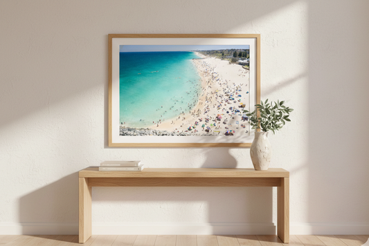 Framed artwork of a beach scene on a wall with a wooden bench below.