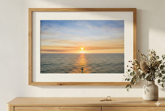 Framed artwork of a sunset over water on a wall above a wooden console table.