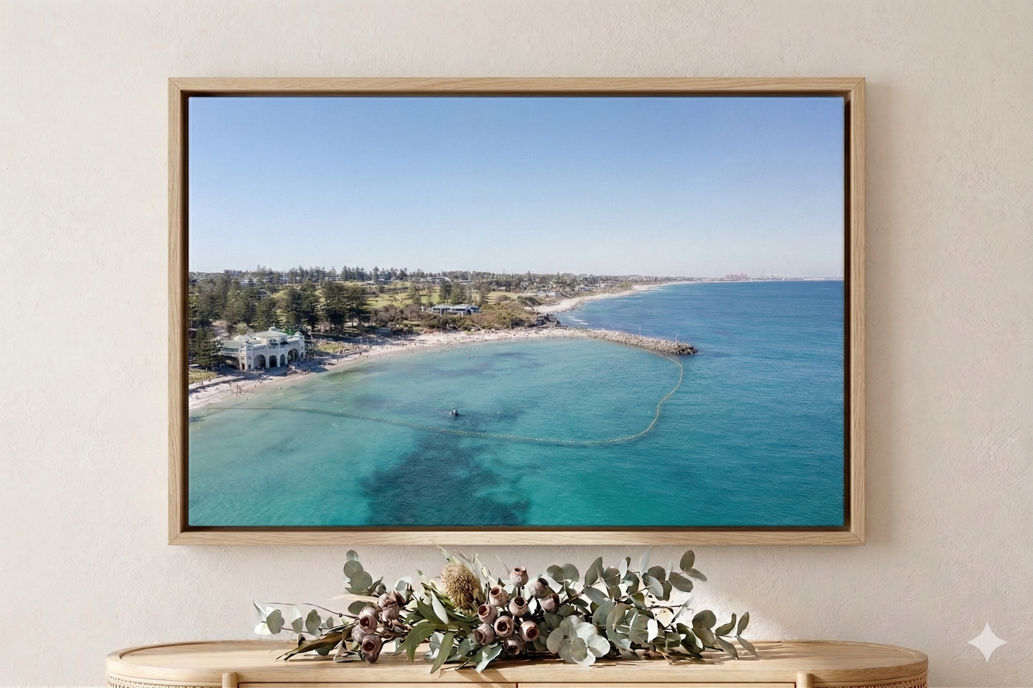 Framed artwork of a beach scene on a wall with decorative plants below.