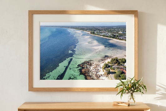 Framed photograph of a coastal landscape on a wall above a wooden console table.