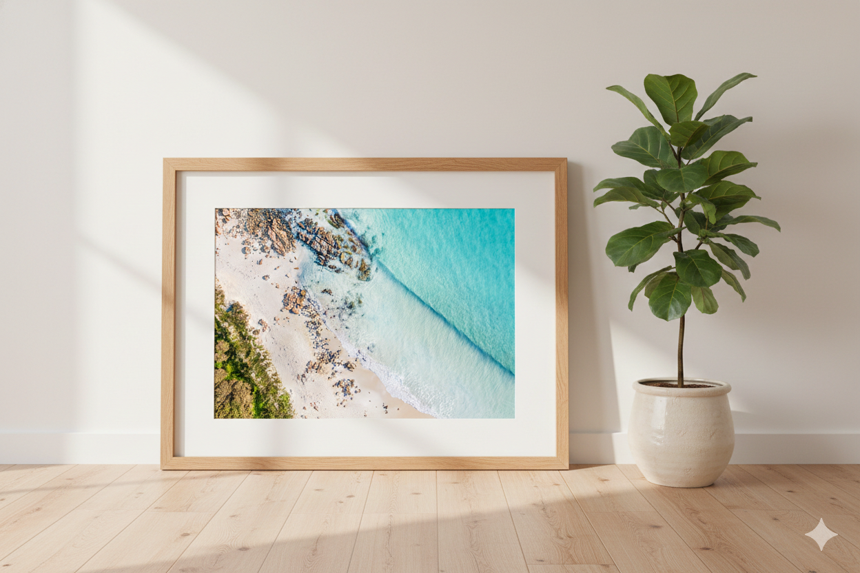 Framed artwork of a beach scene on a wall next to a potted plant.
