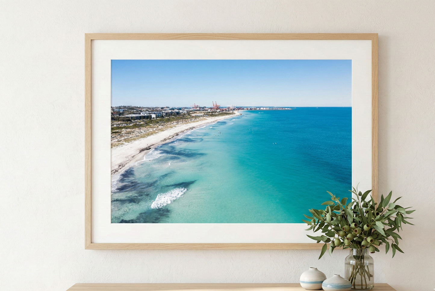 Framed beachscape print on a wall above a wooden console table with decorative items.