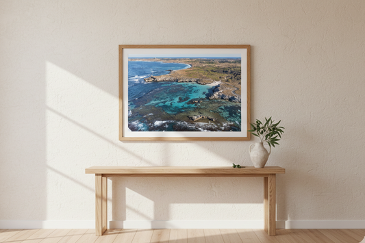 Framed artwork of a coastal scene on a wall above a wooden console table.
