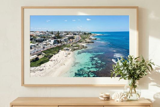Framed photograph of a coastal scene with a beach and ocean on a wall above a wooden console table.