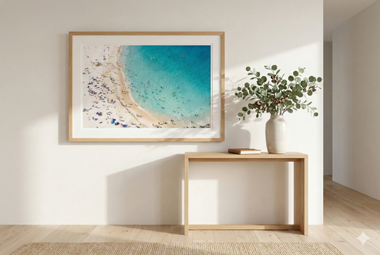 Framed beach print on a wall above a wooden console table with a vase of flowers.