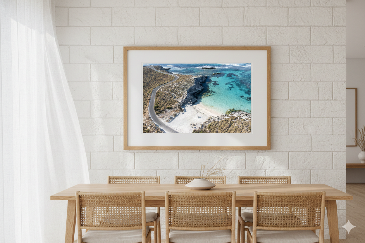 Framed artwork of a coastal scene above a dining table with chairs.