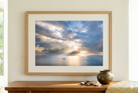 Framed artwork of a sunset over water on a wall above a wooden table.