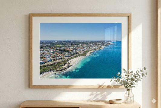Framed artwork of a coastal scene on a wall with a wooden shelf below.