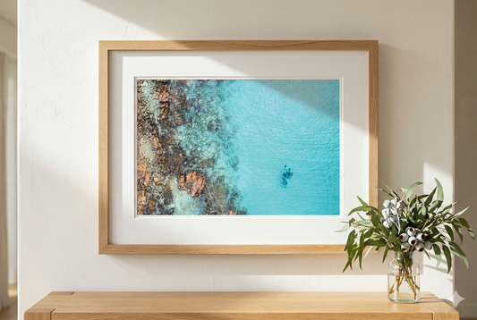 Framed artwork of a coastal scene with a wooden frame on a white wall.