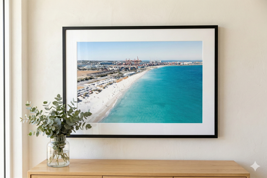 Framed beachscape print on a wall above a wooden console table with a vase of greenery.