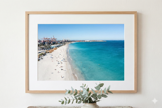 Framed beach scene with clear blue water and white sand, displayed on a light wall.