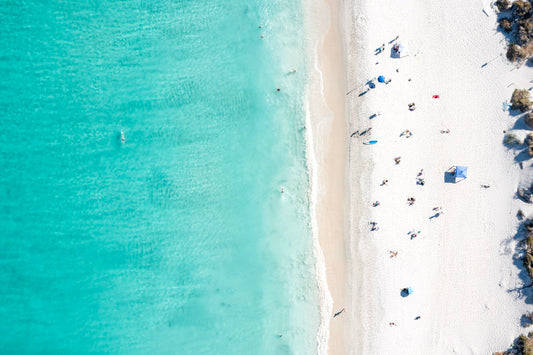 Top-down view of a beach with clear blue water and white sand.