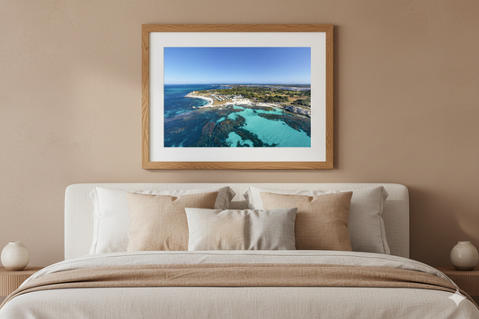 Framed artwork of a coastal scene above a bed with beige bedding.