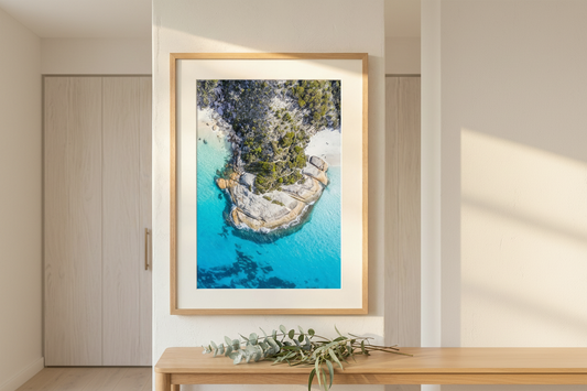 Framed artwork of a coastal landscape with blue water and greenery, displayed on a wall.