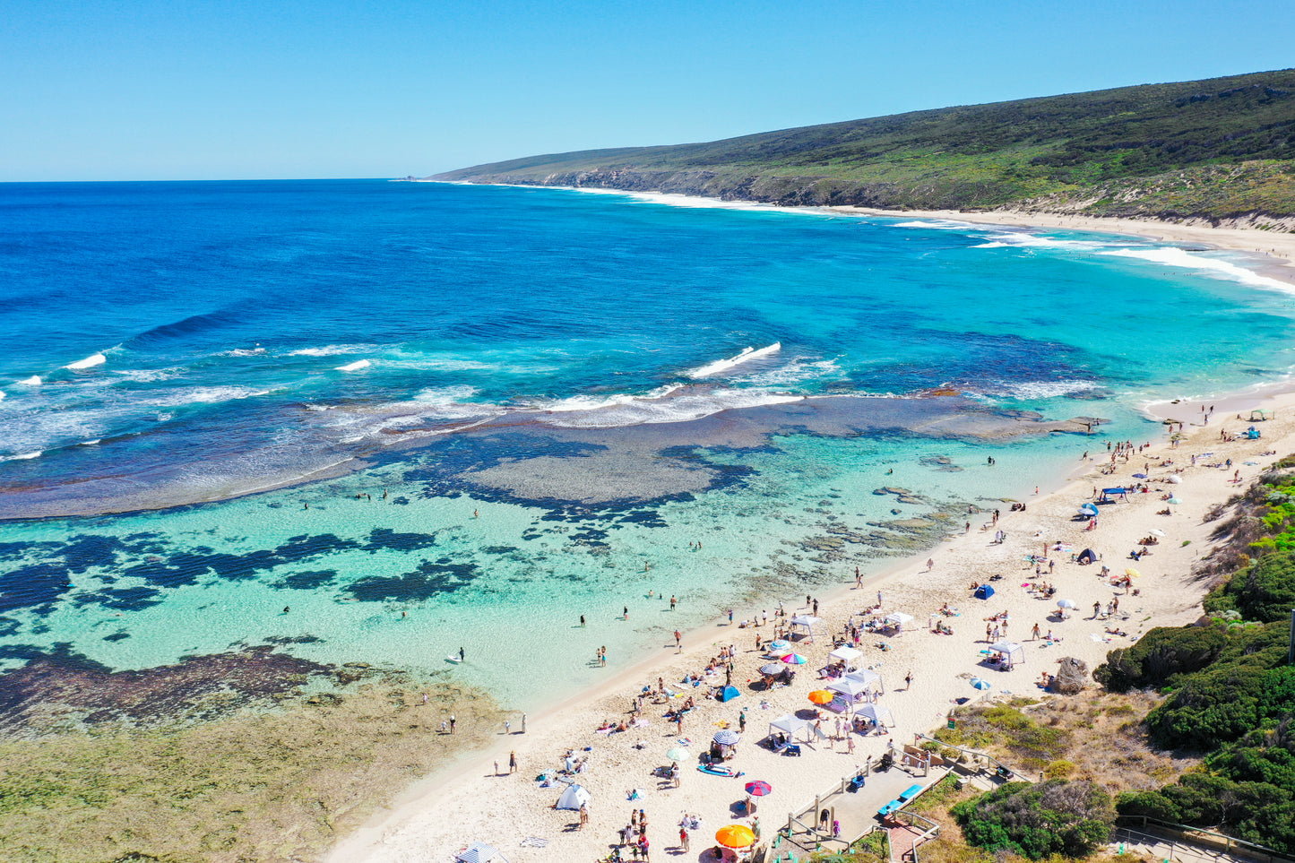 A fine art print of a beach scene with clear blue water, greenery, and people enjoying the sun and surf.