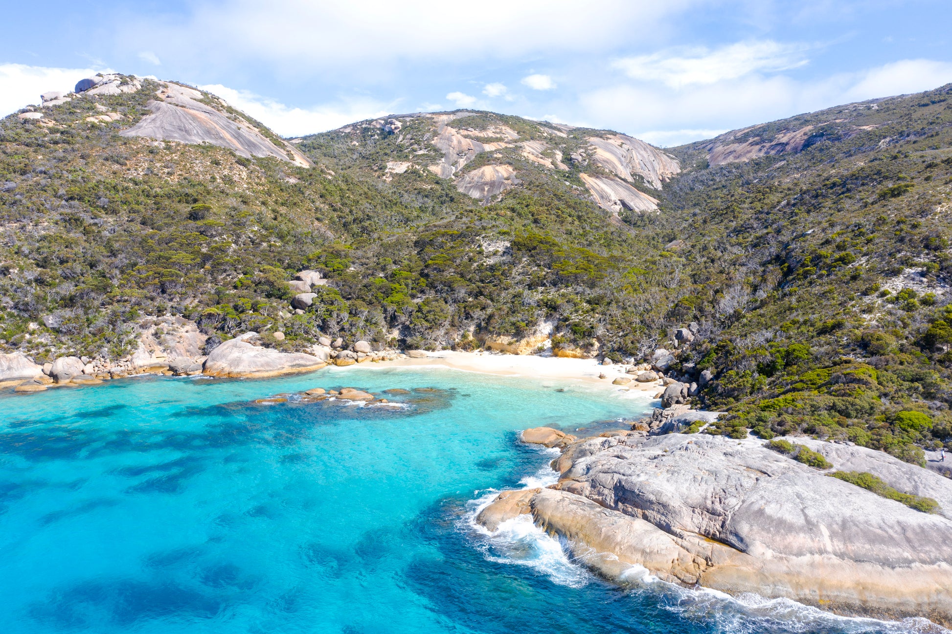 Coastal landscape with clear blue water, rocky shore, and green mountains.