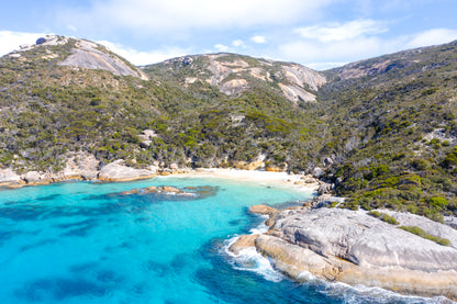 Coastal landscape with clear blue water, rocky shore, and green mountains.