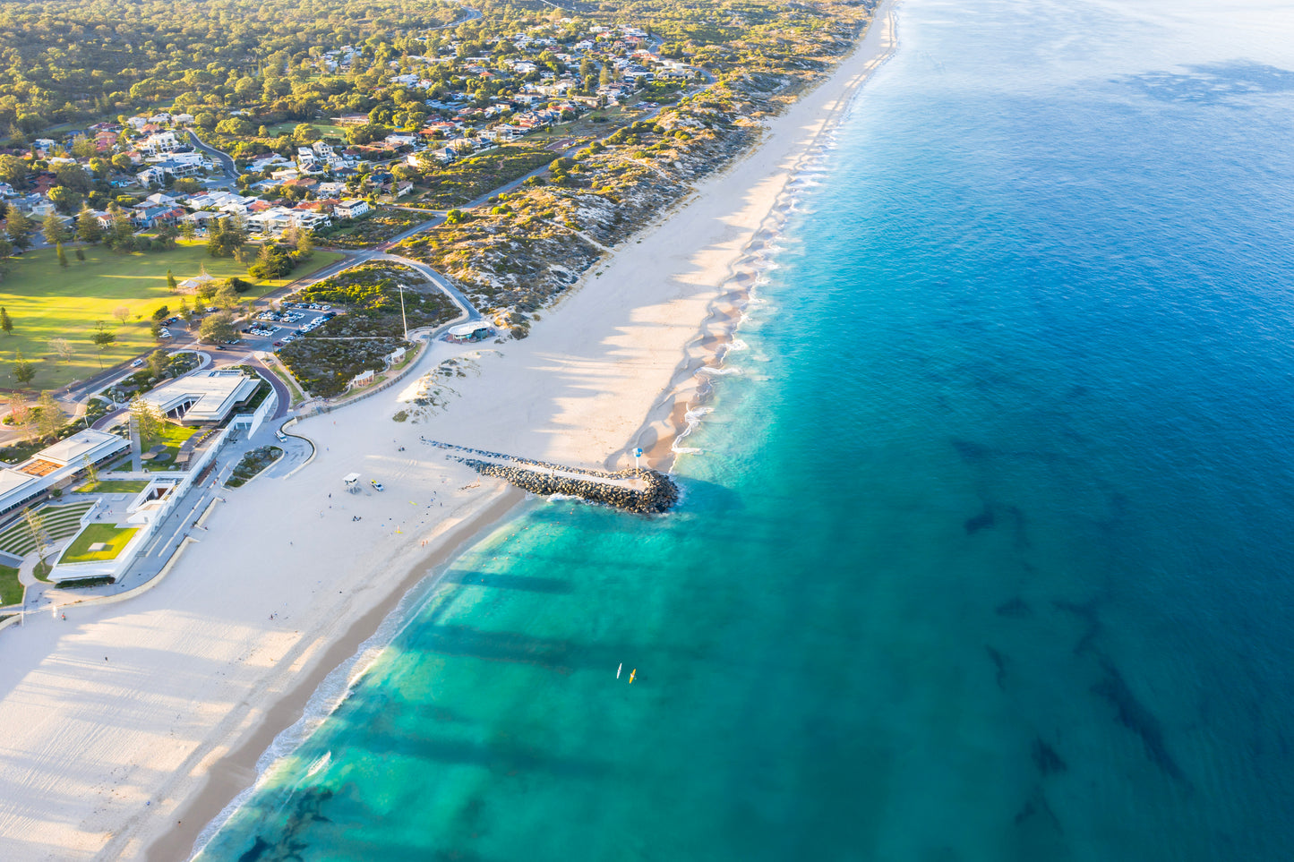 Aerial view of a beach with clear blue water and a coastal town.