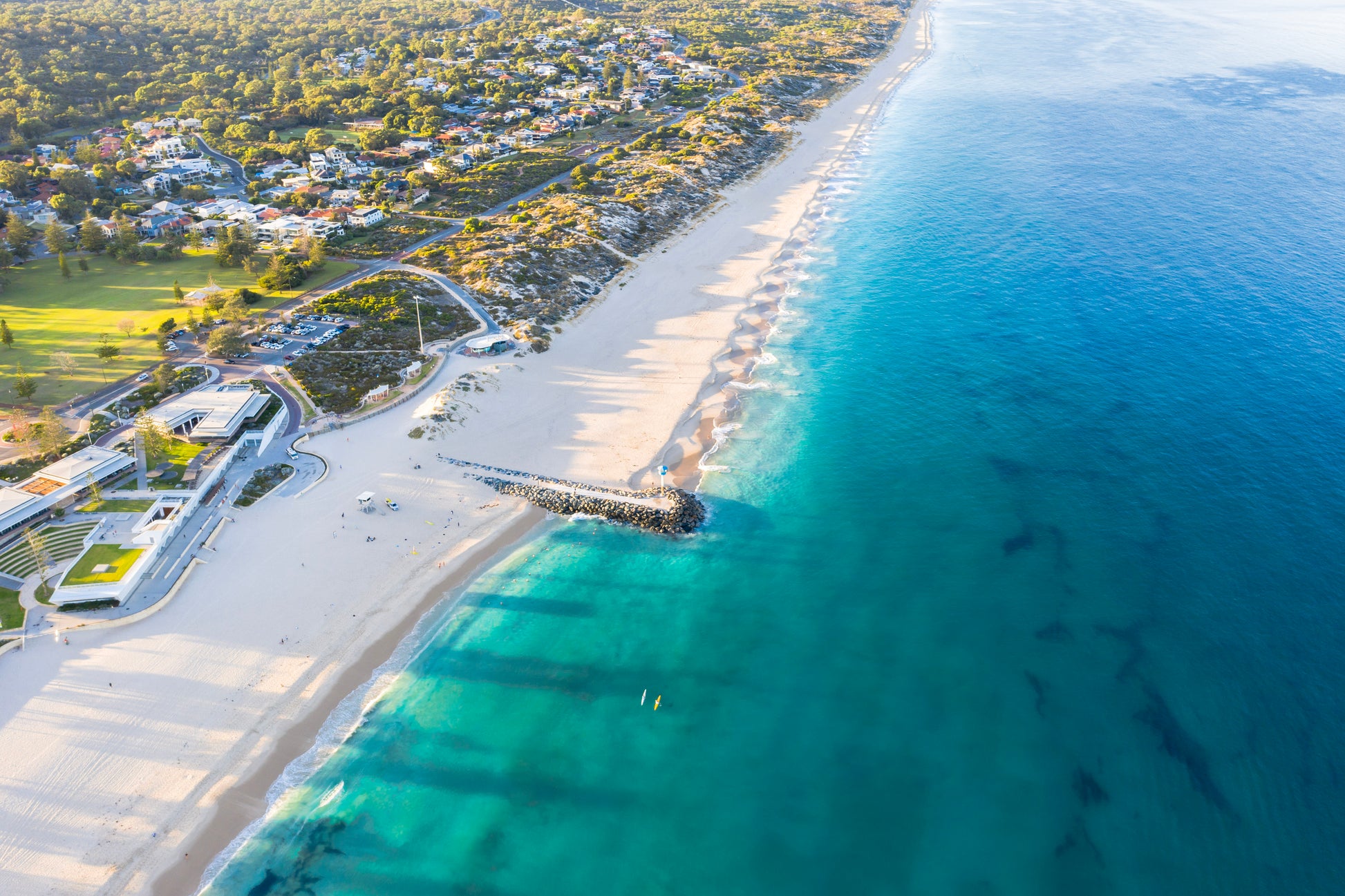 Aerial view of a beach with clear blue water and a coastal town.