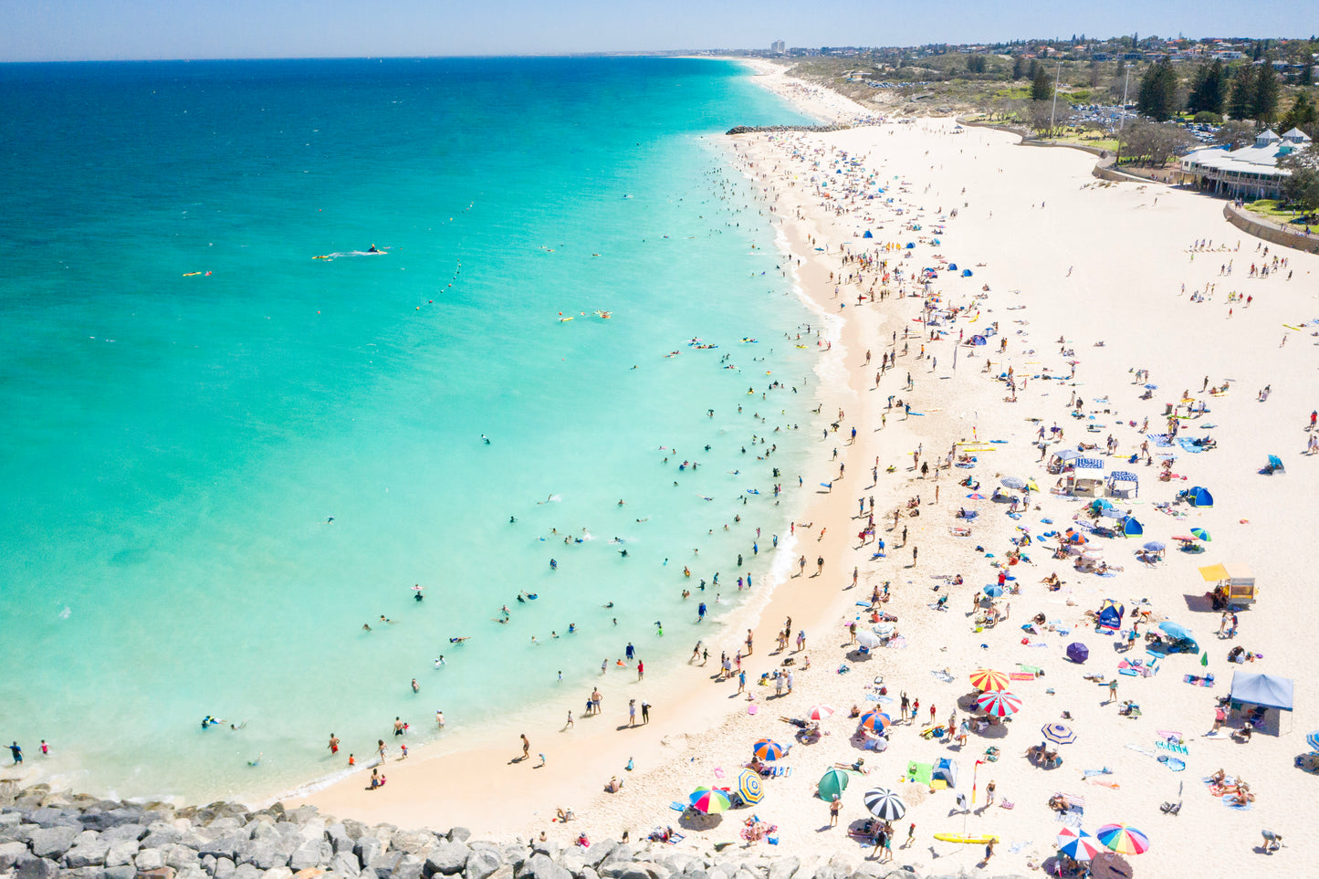 Beach scene with clear blue water and people enjoying the sun on a sandy shore.