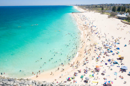 Beach scene with clear blue water and people enjoying the sun on a sandy shore.