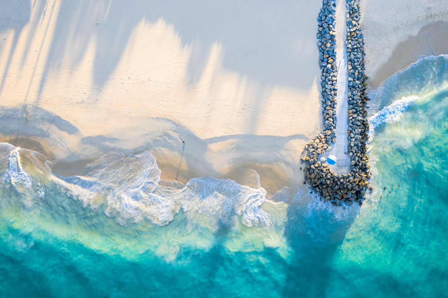 Aerial view of a rocky shoreline with turquoise water and white foam.