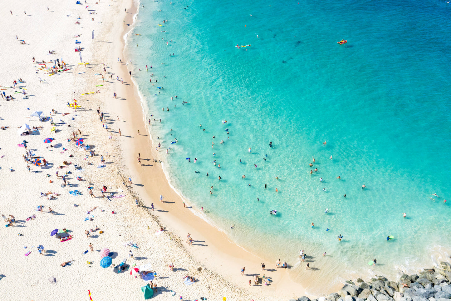 Beach scene with people and umbrellas on a sandy shore with clear blue water.