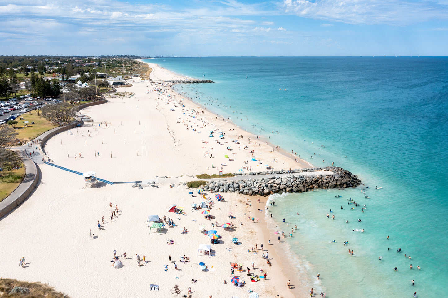 Beach scene with people enjoying the sun and water, clear blue sky above.