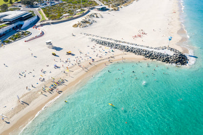 Aerial view of a beach with people, umbrellas, and kayaks in clear blue water.
