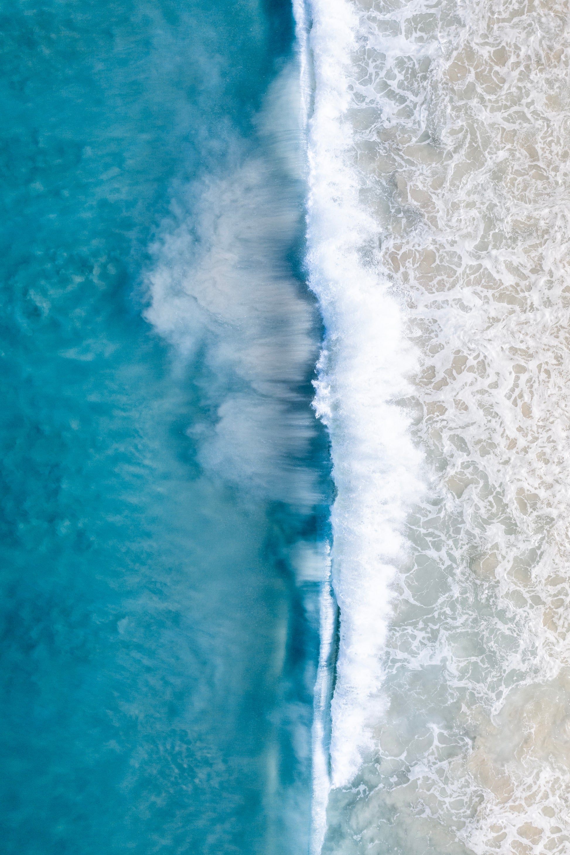 Top-down view of ocean waves crashing onto a beach