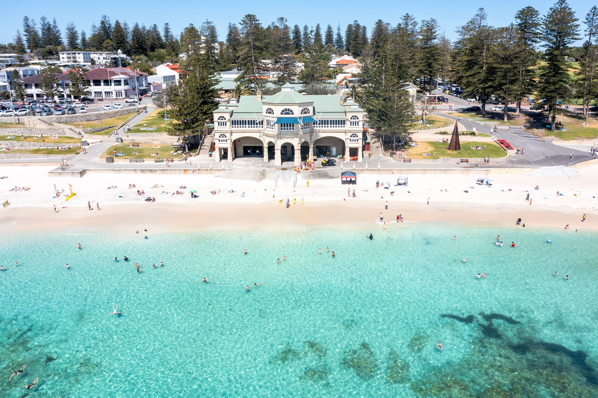 Aerial view of a beach with clear blue water and a building in the background.