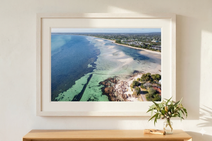 Framed aerial view of a coastal landscape on a wall above a wooden console table with a vase.