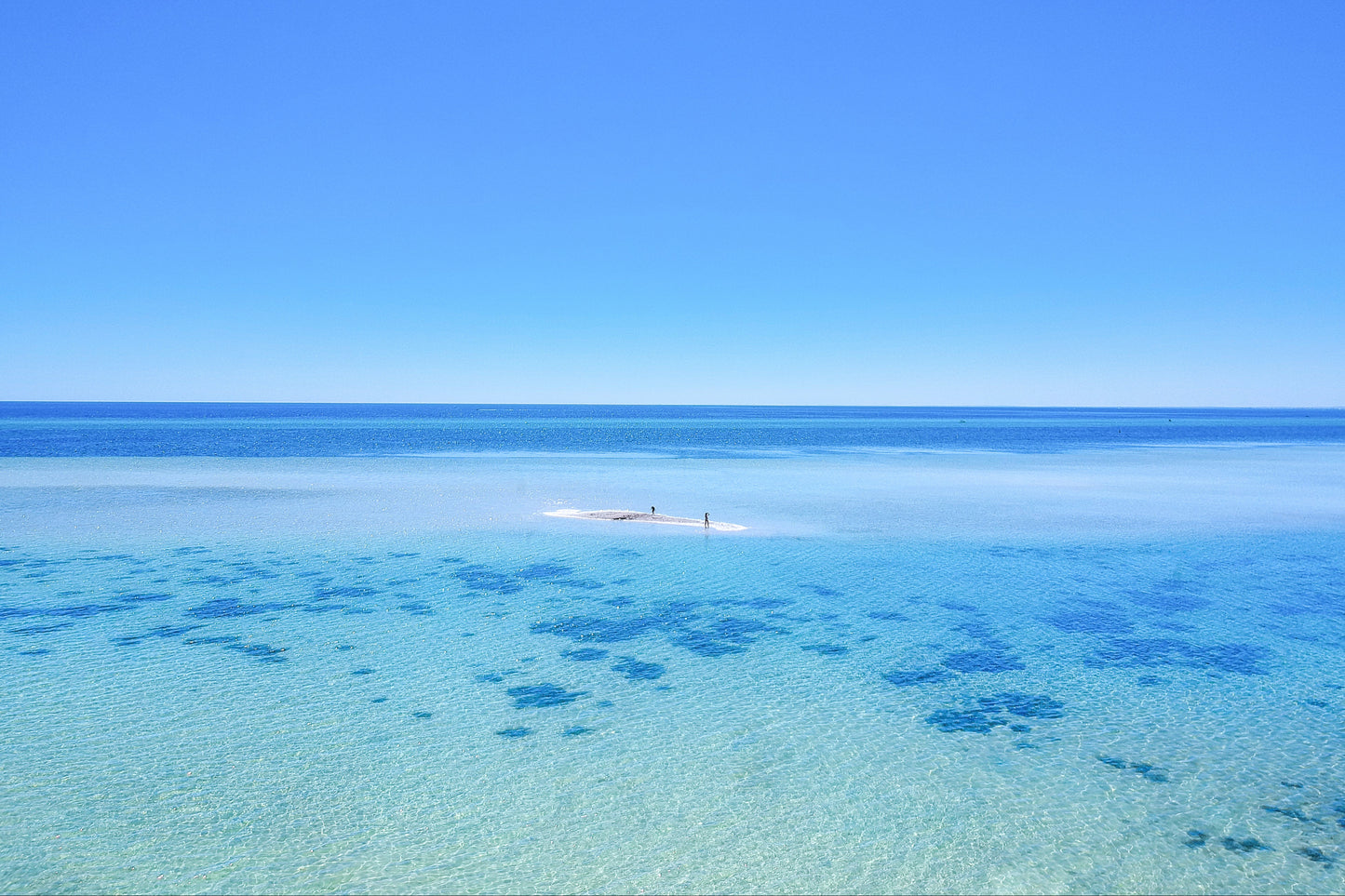 Clear blue water with a small boat in the distance under a clear sky