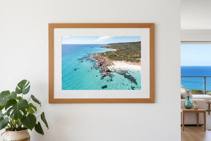 Framed photograph of a coastal scene on a white wall with a plant and part of a room visible. Eagle Bay WA Dunsborough.