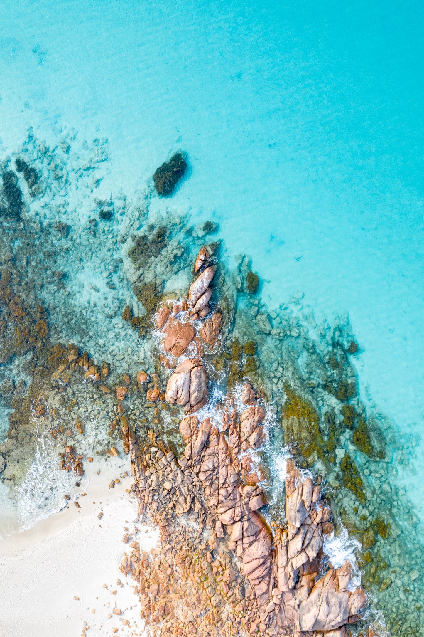 Top-down view of a rocky coastline with clear blue water.