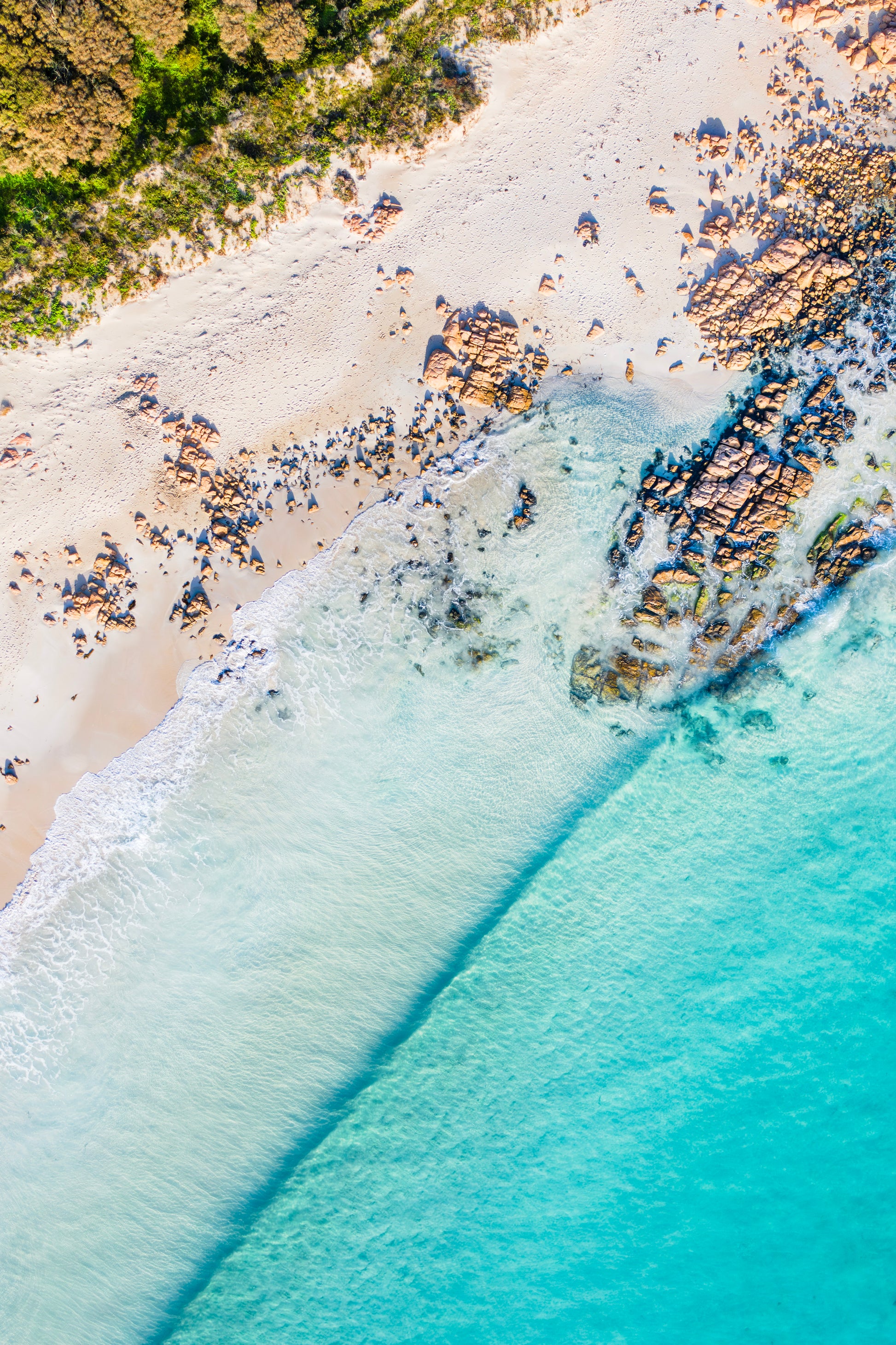 Aerial view of a beach with clear blue water and rocky shoreline.