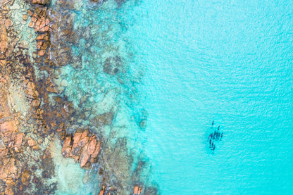 Aerial view of a person kayaking in clear blue water near rocky shores.
