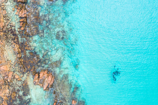 Aerial view of a person kayaking in clear blue water near rocky shores.