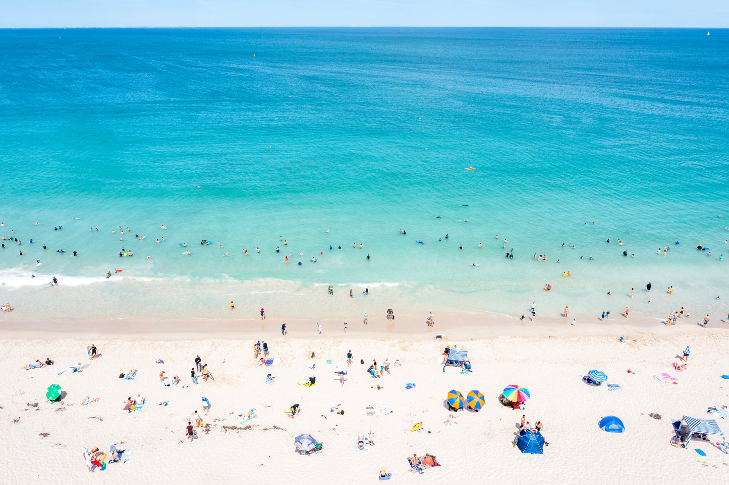 Beach scene with people and umbrellas under a clear blue sky.
