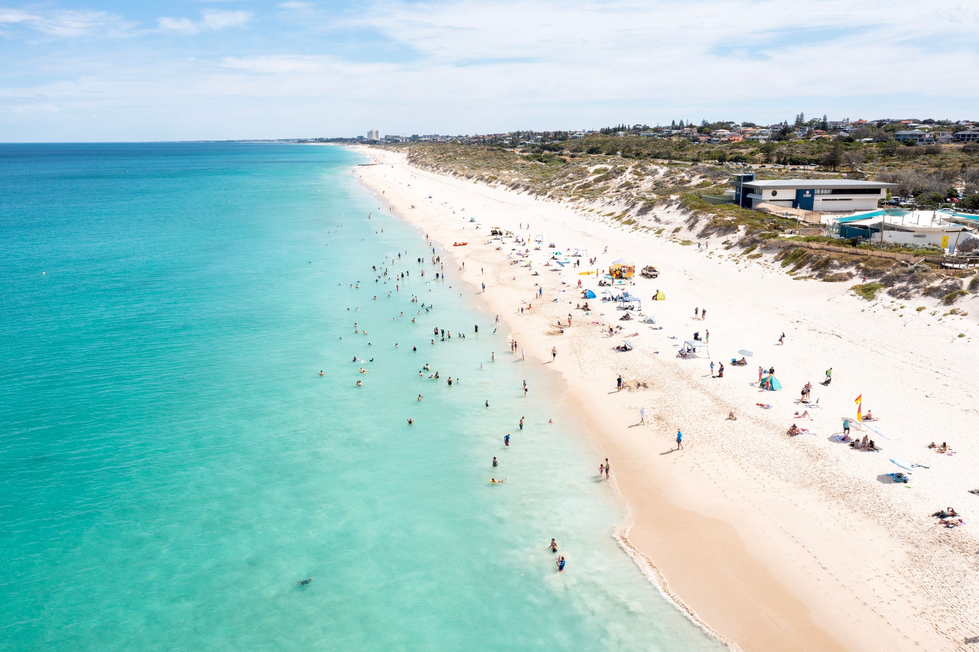 Beach scene with clear blue water and white sand, people enjoying the beach.
