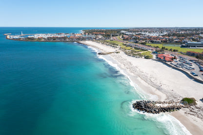 Aerial view of a coastal area with clear blue water, sandy beach, and buildings.
