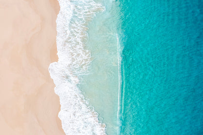 Top-down view of a beach with turquoise water and white waves.