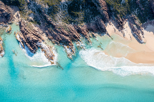 Aerial view of a beach with clear turquoise water and rocky shoreline.