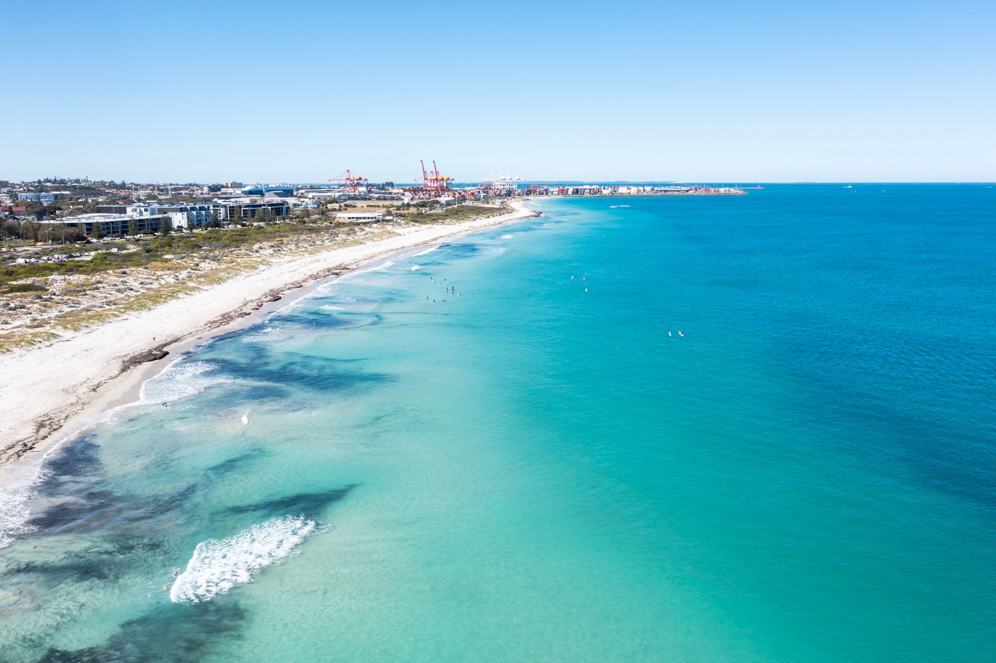 Aerial view of a beach with clear blue water and a cityscape in the distance.
