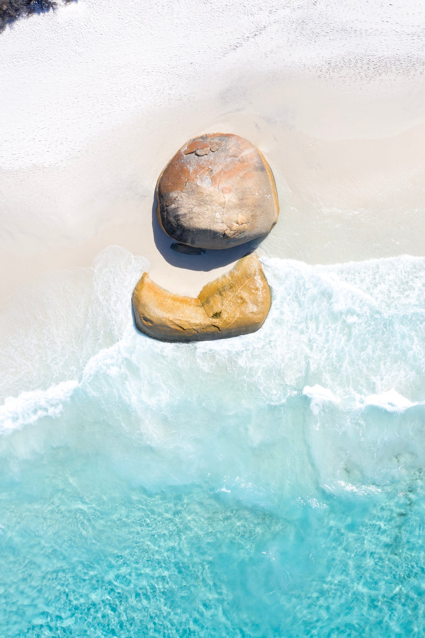 Two stones balanced on top of each other with water and snow in the background