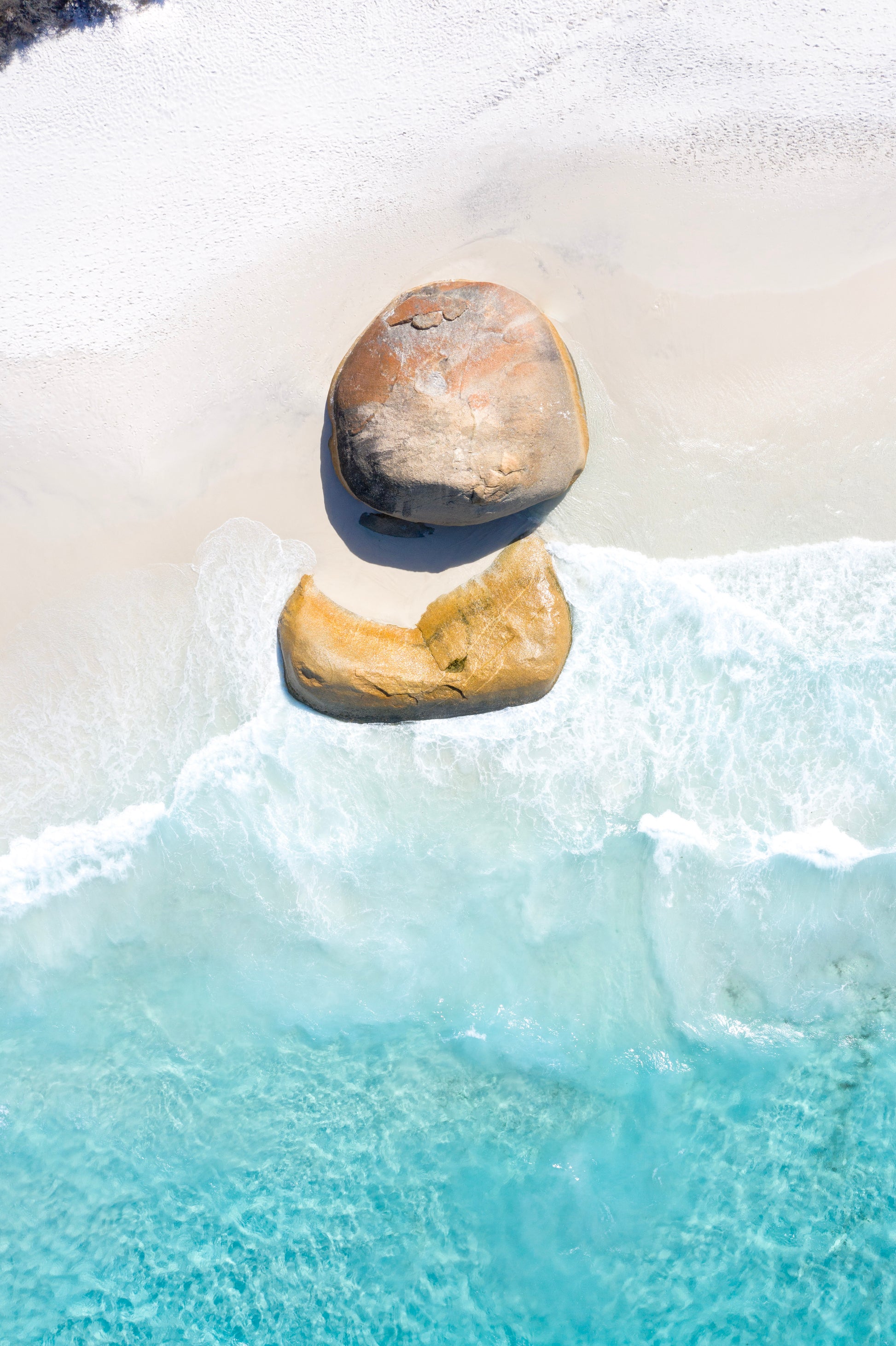 Two stones balanced on top of each other with water and snow in the background