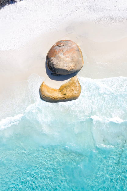 Two stones balanced on top of each other with water and snow in the background