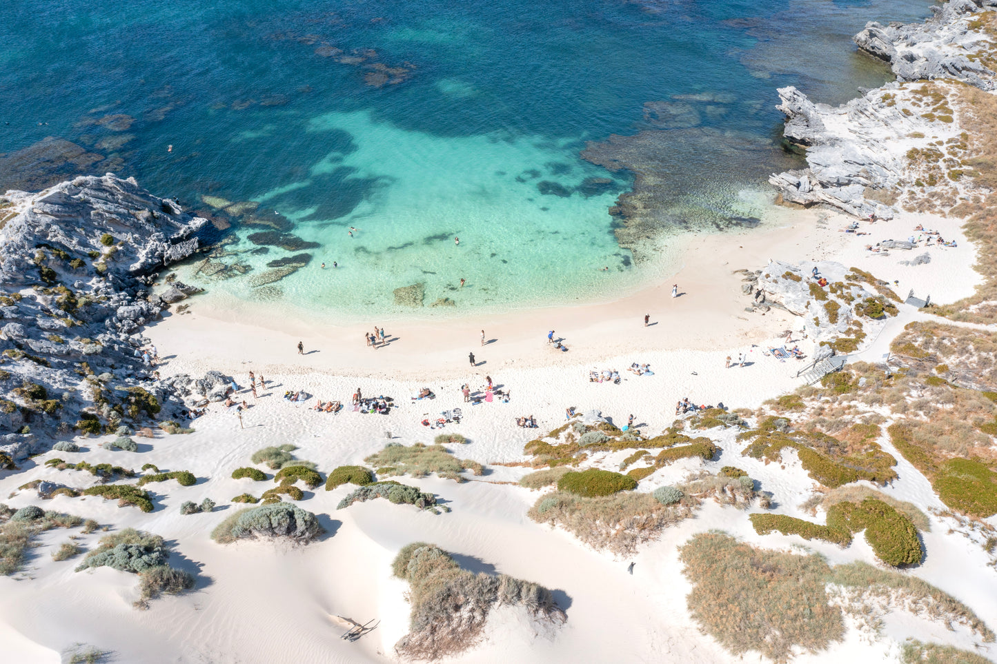 Beach scene with people enjoying the water and sand, surrounded by greenery.
